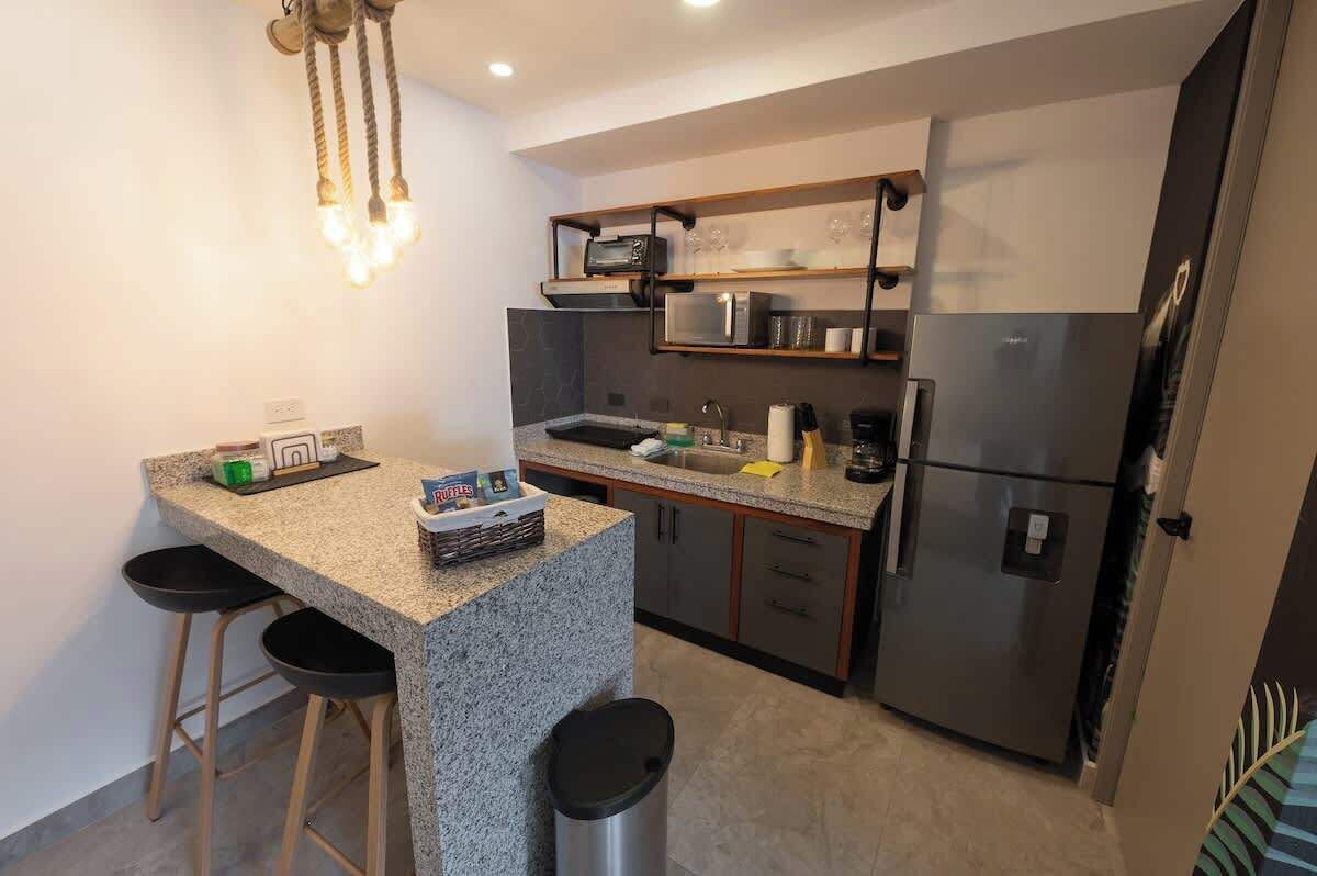 Cocina compacta con encimera de granito, microondas, refrigerador y lámpara colgante.