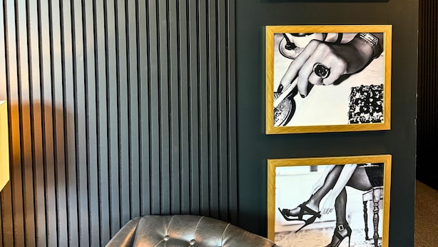 Une pièce avec un mur de couleur sombre, un fauteuil en cuir capitonné et trois tableaux encadrés.