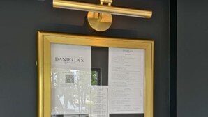 Un panneau de menu encadré, avec du texte et un code QR, fixé sur un mur foncé, avec une barre horizontale de couleur or au-dessus.