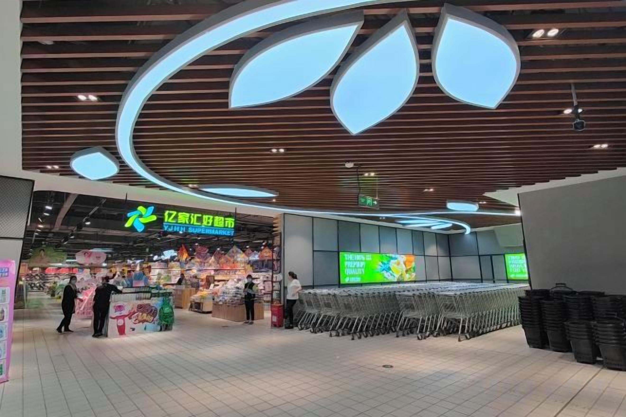 A modern shopping area with a prominent store entrance, a seating area with a long bench, and a ceiling with a unique light fixture.