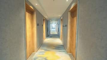 A hotel corridor with doors on both sides, a carpet with a pattern, and a light source at the end.
