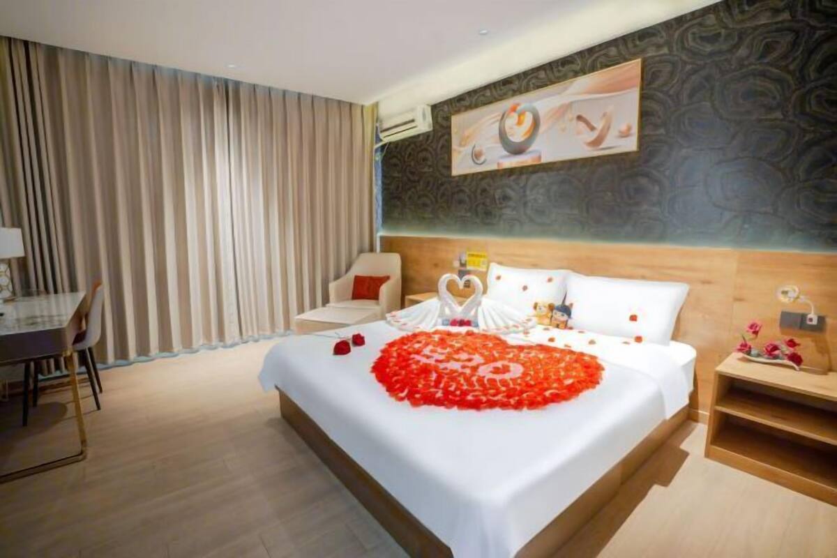 A hotel room with a neatly made bed, a dining area, and a large window with curtains.
