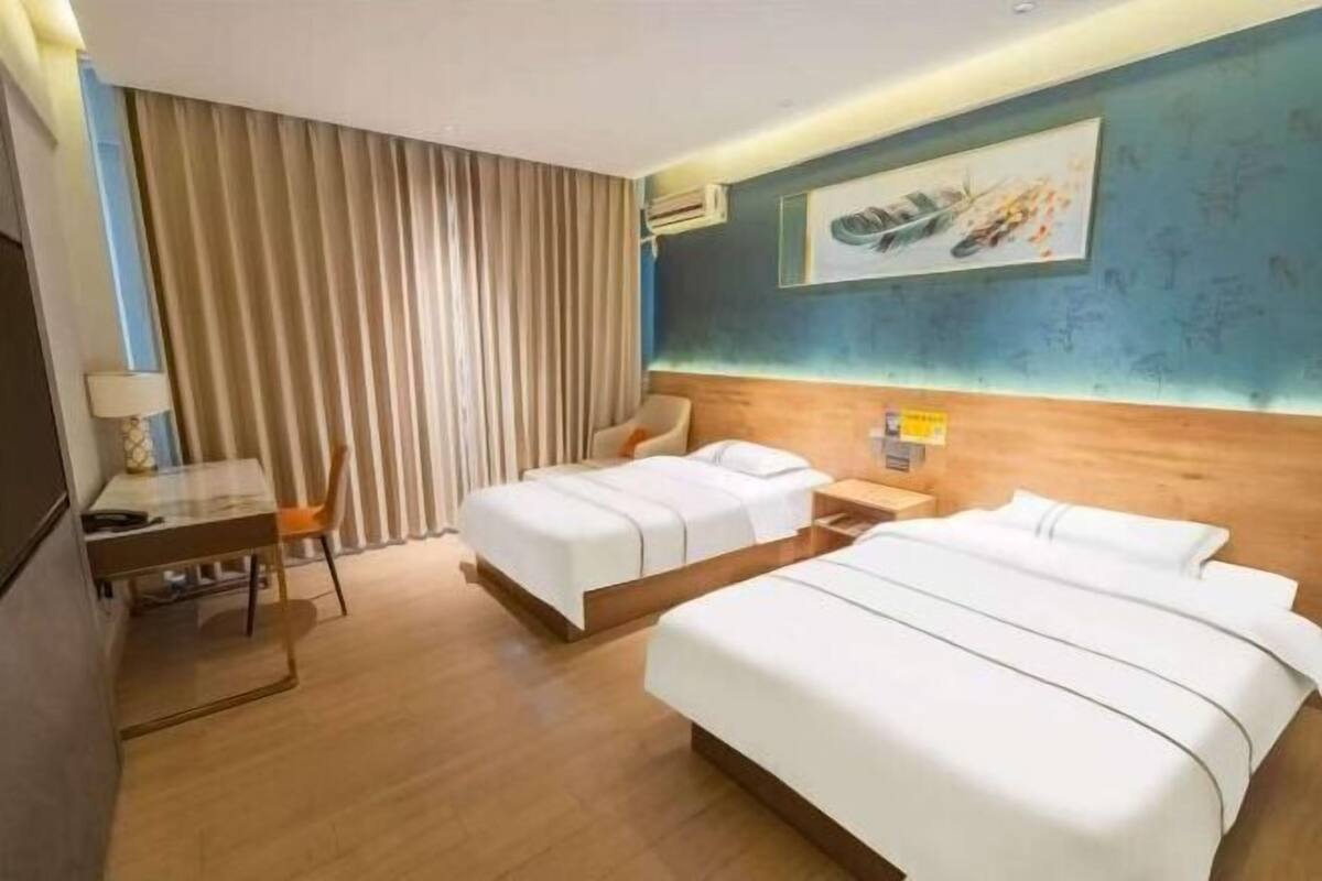 A hotel room with two beds, a desk, a chair, a lamp, and a large window with curtains.