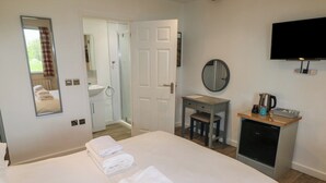 Une chambre d’hôtel avec un lit, un bureau, un miroir, une télévision et une salle de bain visible à travers une porte ouverte.
