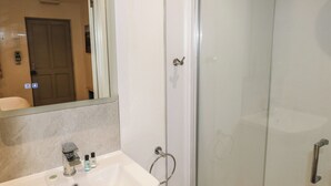 Une salle de bain avec un lavabo blanc, un miroir et une cabine de douche en verre.