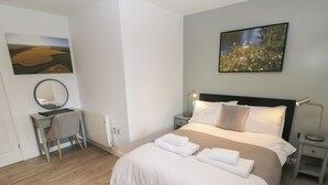 Un dormitorio con una cama grande, un escritorio con silla, un espejo redondo y dos cuadros en las paredes.