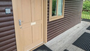 Una cabaña de madera con una puerta color beige, una ventana y un porche con felpudo.