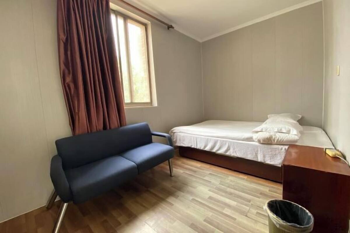 A room with a bed, a blue sofa, a window with curtains, and a wooden floor.