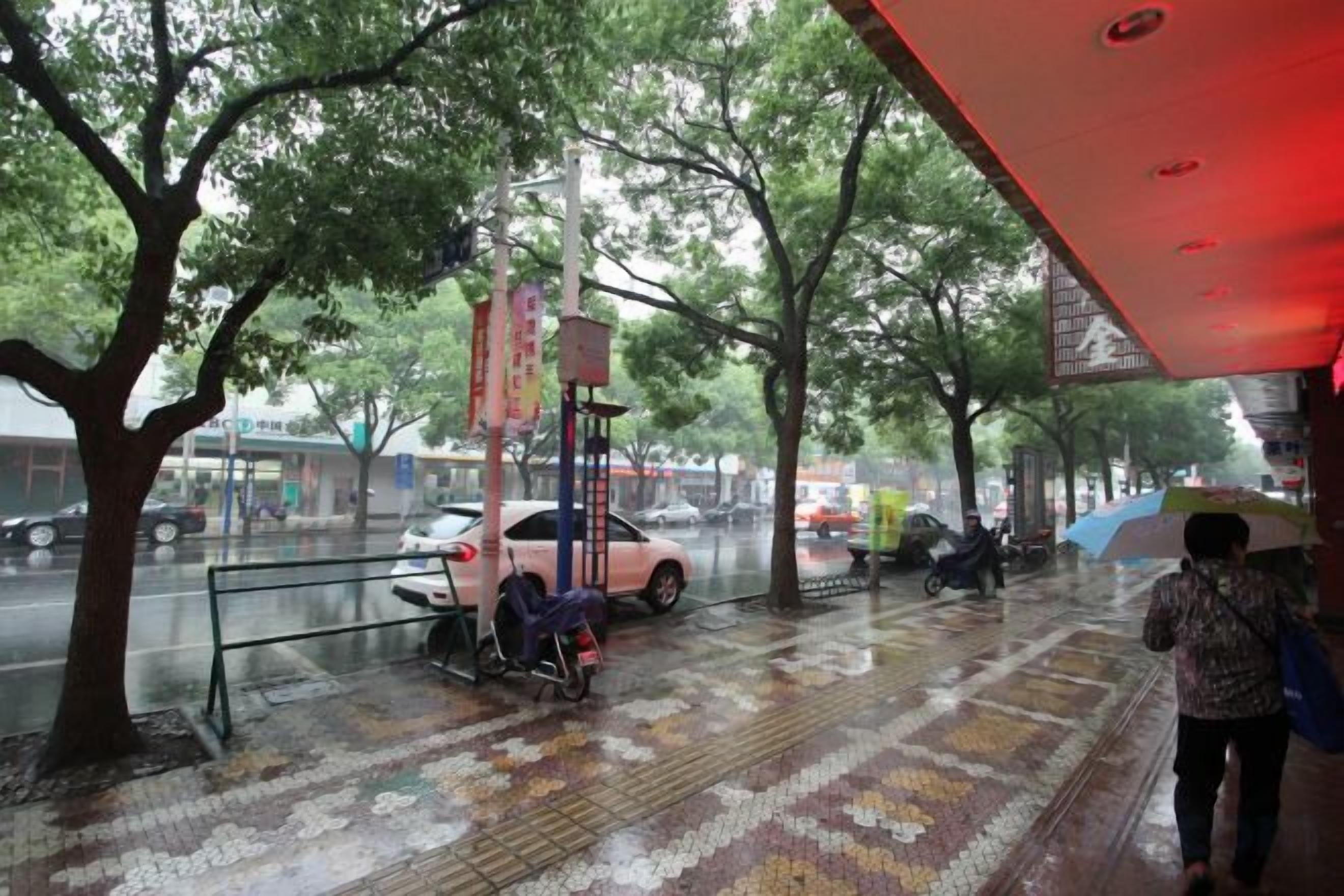 A covered outdoor area with a tiled floor, trees, and a car parked nearby.
