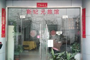 A hotel entrance with a glass door, a red sign above the door, and some potted plants inside. - Xinjiyuan Hostel (Shanghai)
