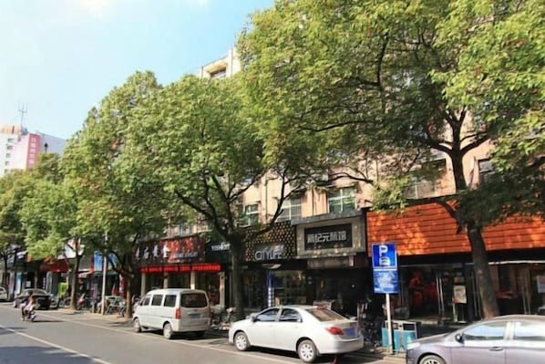 Rua arborizada com edifícios, incluindo uma placa de estacionamento visível.