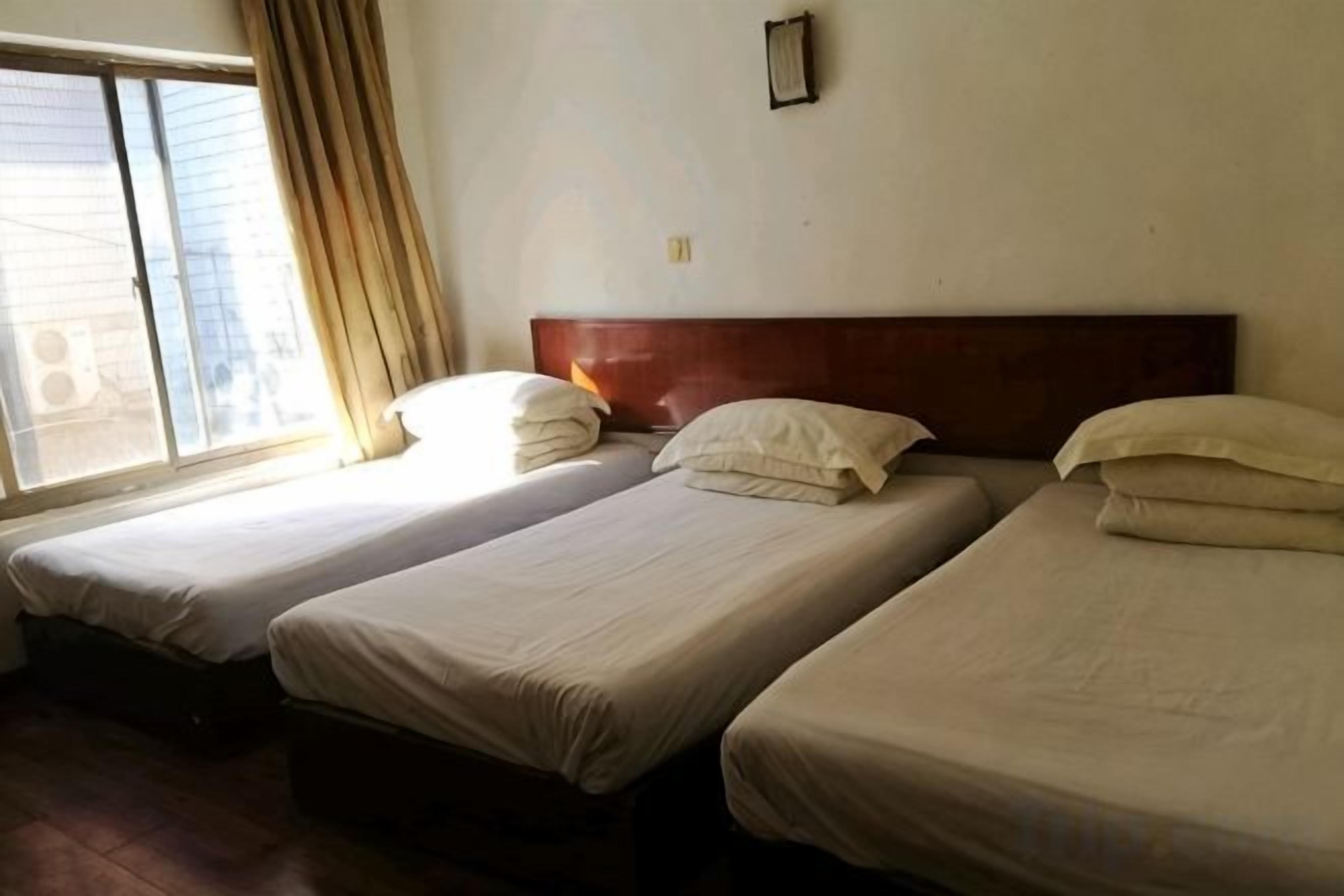 A room with three single beds aligned against a wall, a window with curtains, and a wooden headboard.