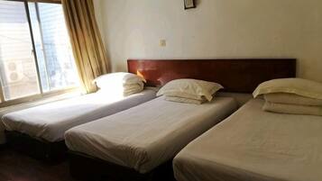 A room with three single beds aligned against a wall, a window with curtains, and a wooden headboard.