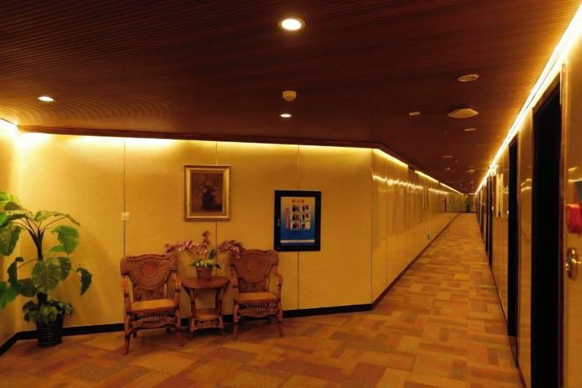 Un corridoio d'hotel con pavimento in legno, un'area salotto con sedie e un tavolo, e quadri appesi alle pareti.