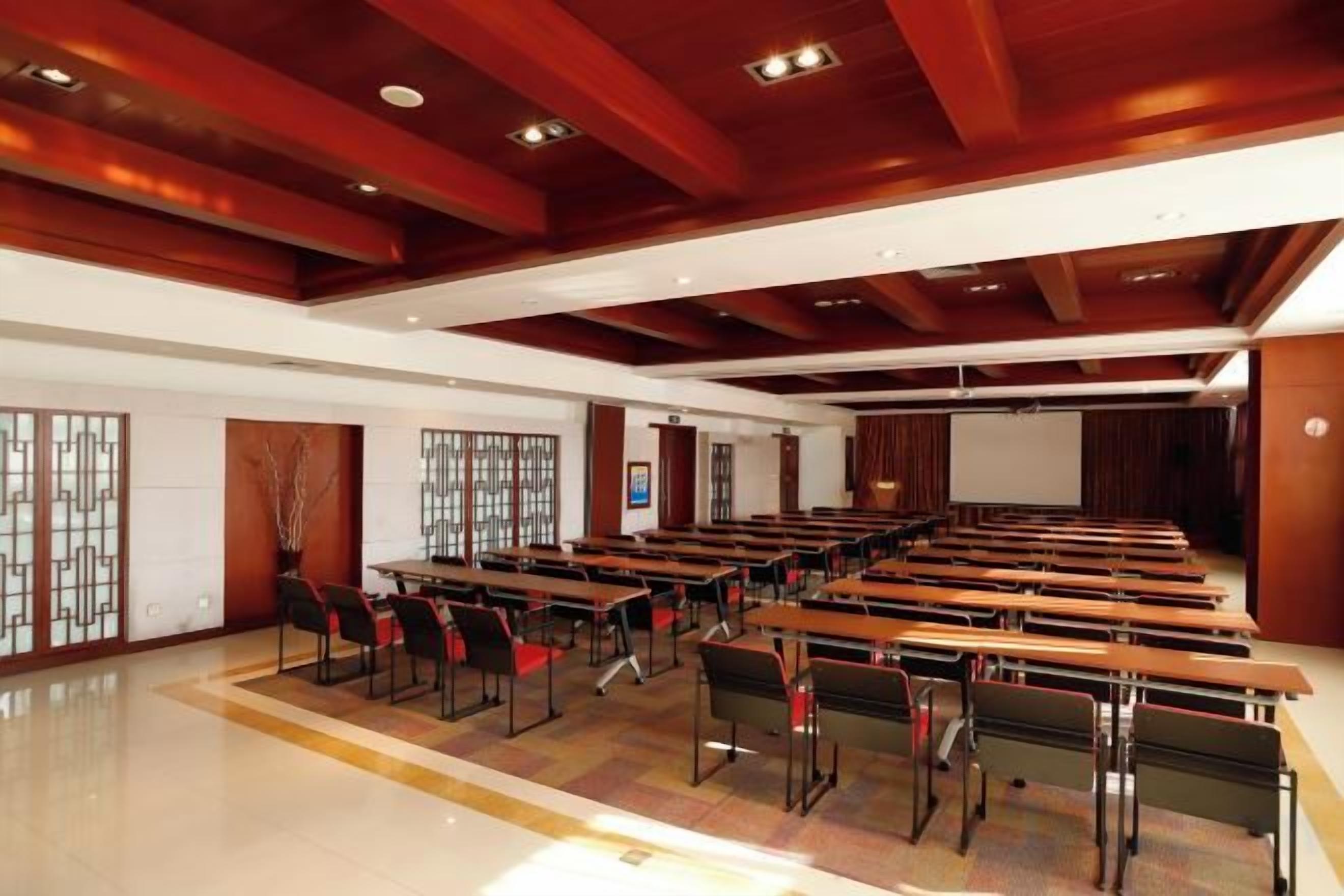 Un salón de conferencias con varias mesas y sillas, vigas de madera en el techo y una pantalla de proyector.