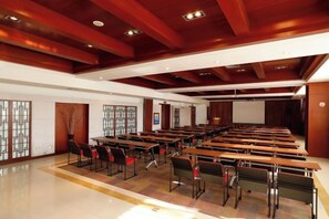 A conference room with multiple tables and chairs, wooden ceiling beams, and a projector screen.