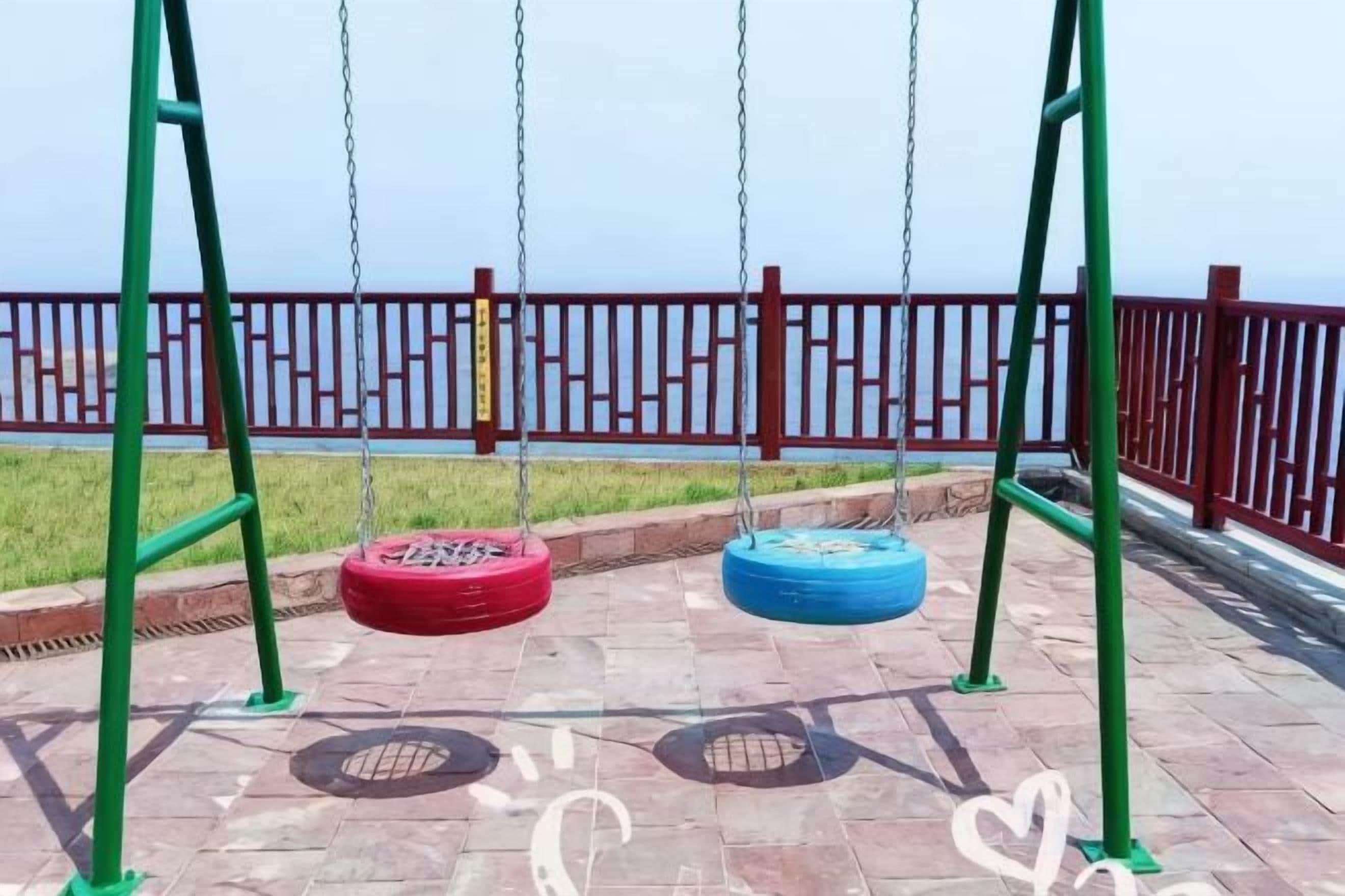 Un parque infantil con columpios y una cerca roja al fondo.