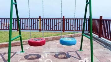 Un parque infantil con columpios y una cerca roja al fondo.