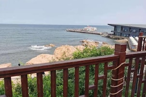 Vista costera con muelle que se adentra al mar, un edificio de diseño moderno y una baranda de madera al frente.