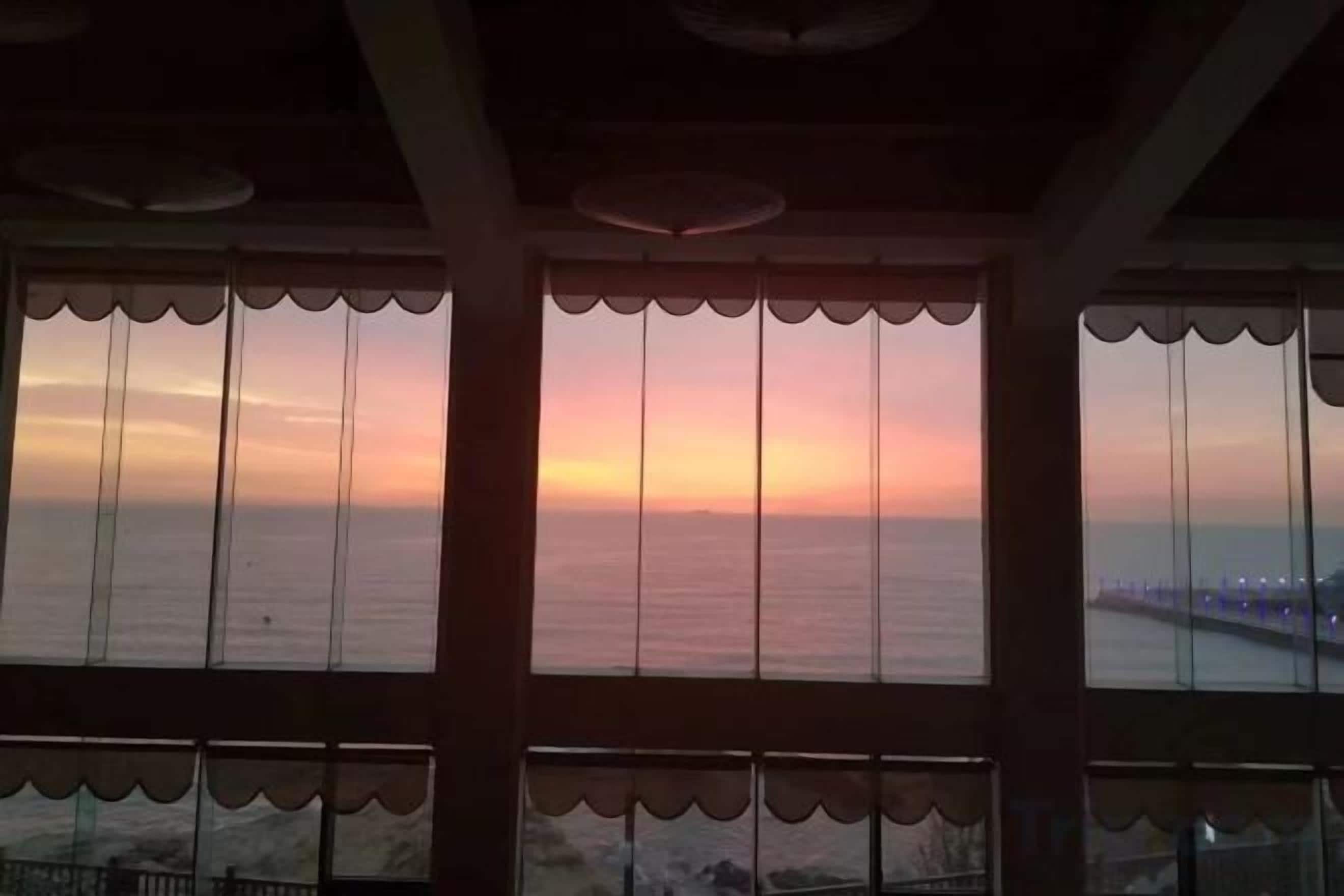 A view through a window with a scalloped design, overlooking a body of water and a distant shoreline.