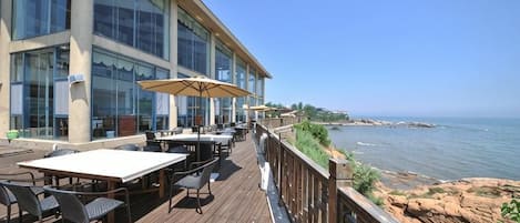 A wooden deck with outdoor seating, overlooking a body of water and a rocky shoreline.