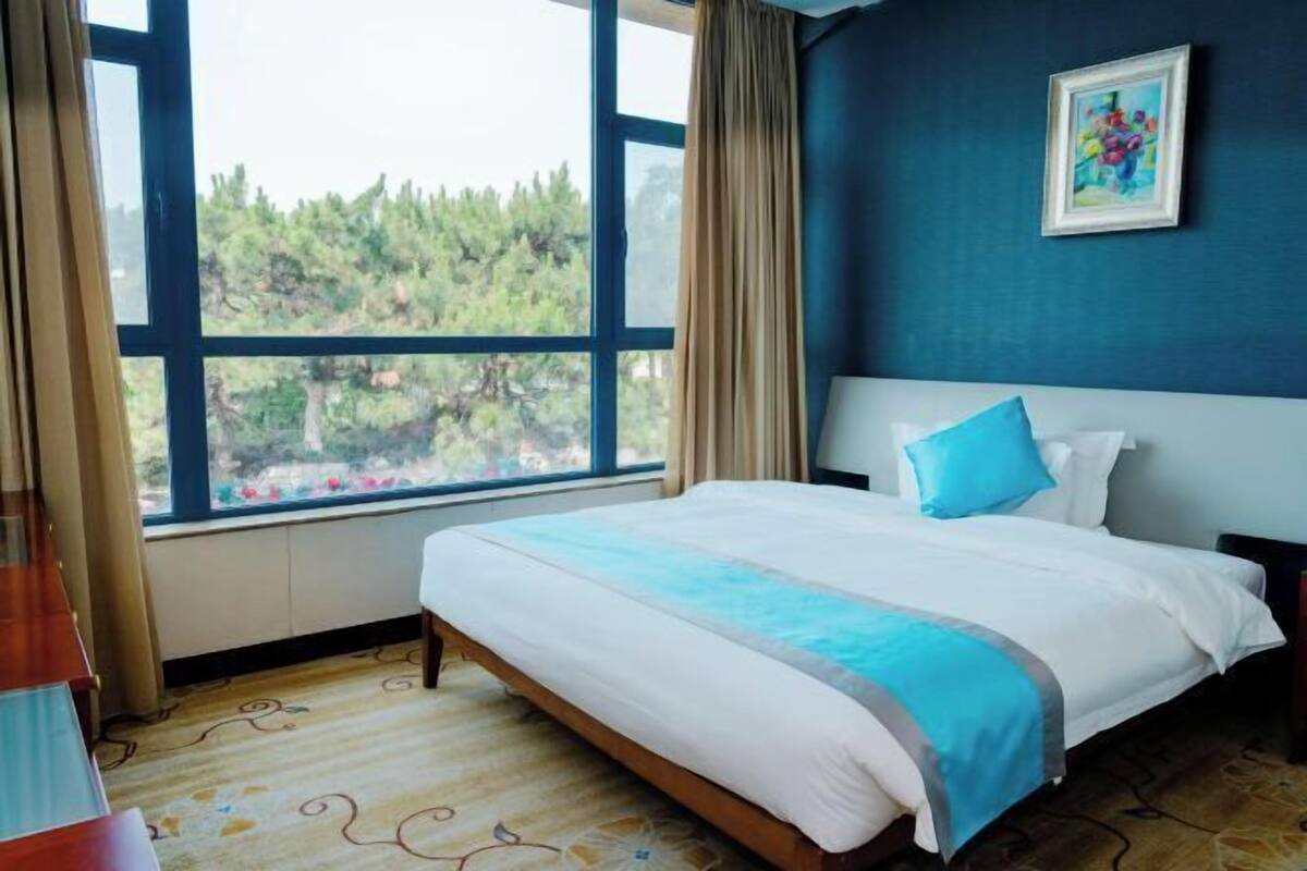 Una camera d'albergo con una grande finestra, un letto con dettagli blu e un quadro appeso al muro.