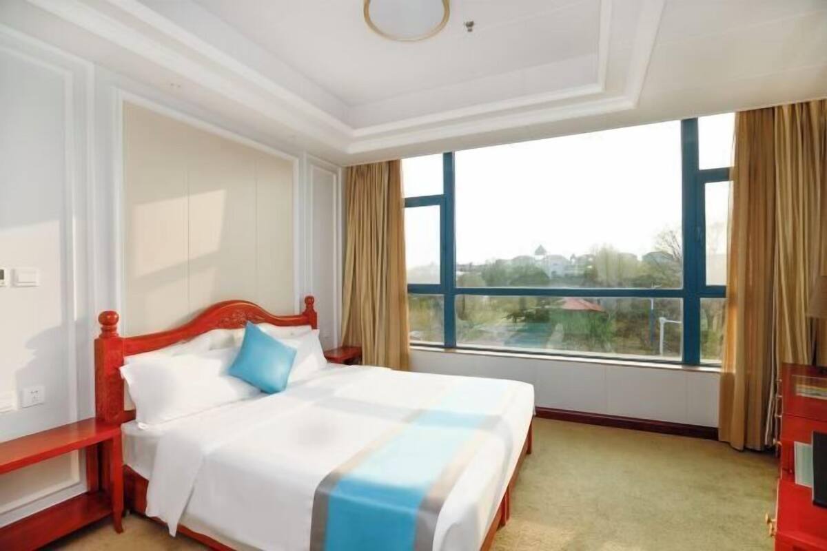Una camera d'albergo con un'ampia finestra, un letto con testiera rossa e un mobile di colore rosso.