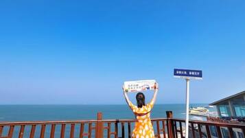 A person holding a sign with text, a railing, and a view of the sea.