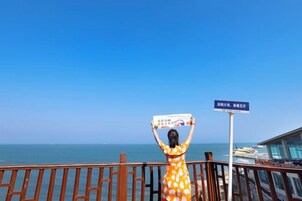 Una persona sostiene un cartel, una barandilla y vistas al mar.