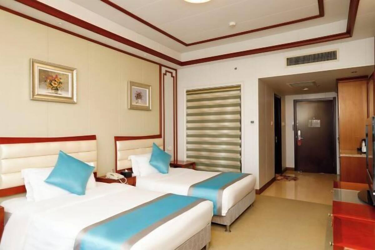Camera d'albergo con due letti, una testiera in legno, un grande specchio, una parete di colore rosso e una porta che dà su un corridoio.