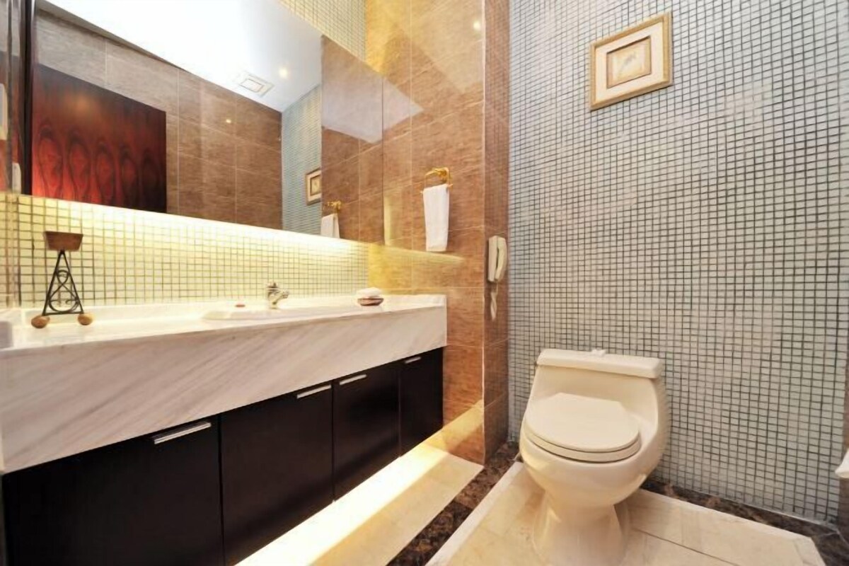 Un bagno moderno con un lavabo in marmo, mobili scuri, un water e una parete rivestita in piastrelle.