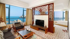A living room with a large TV, wooden furniture, and a view of the sea. - Beidaihe Bei Hua Yuan Sea View Hotel (Beidaihe Biluo Tower) (Qinhuangdao)