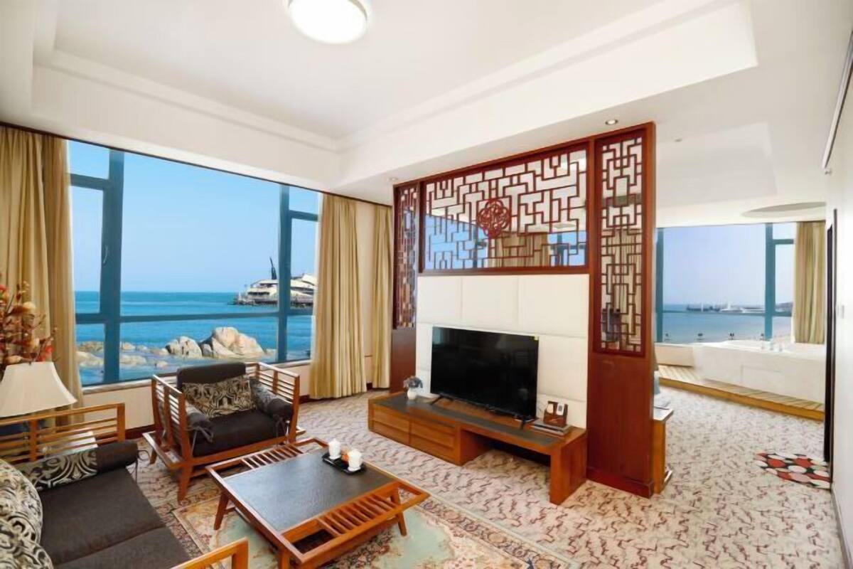 Un soggiorno con una grande TV, arredi in legno e vista mare.
