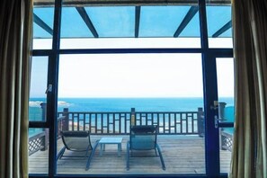 A room with a large window overlooking the ocean, two chairs, a small table, and a wooden deck. - Beidaihe Bei Hua Yuan Sea View Hotel (Beidaihe Biluo Tower) (Qinhuangdao)