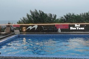 A swimming pool with a tiled edge, surrounded by a deck with chairs and a table. - Beidaihe Bei Hua Yuan Sea View Hotel (Beidaihe Biluo Tower) (Qinhuangdao)