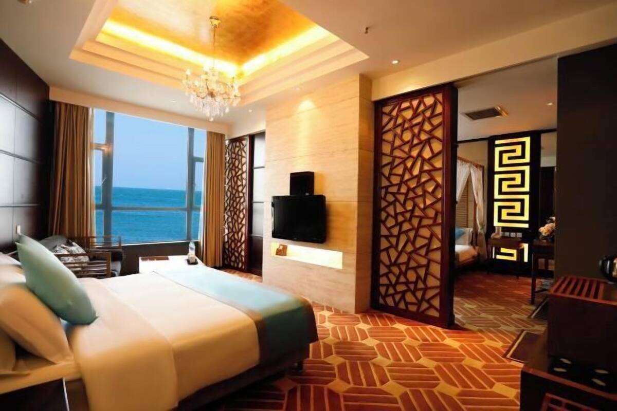 Una camera d'albergo con un letto grande, una TV, vista sul mare e un divisorio decorativo.