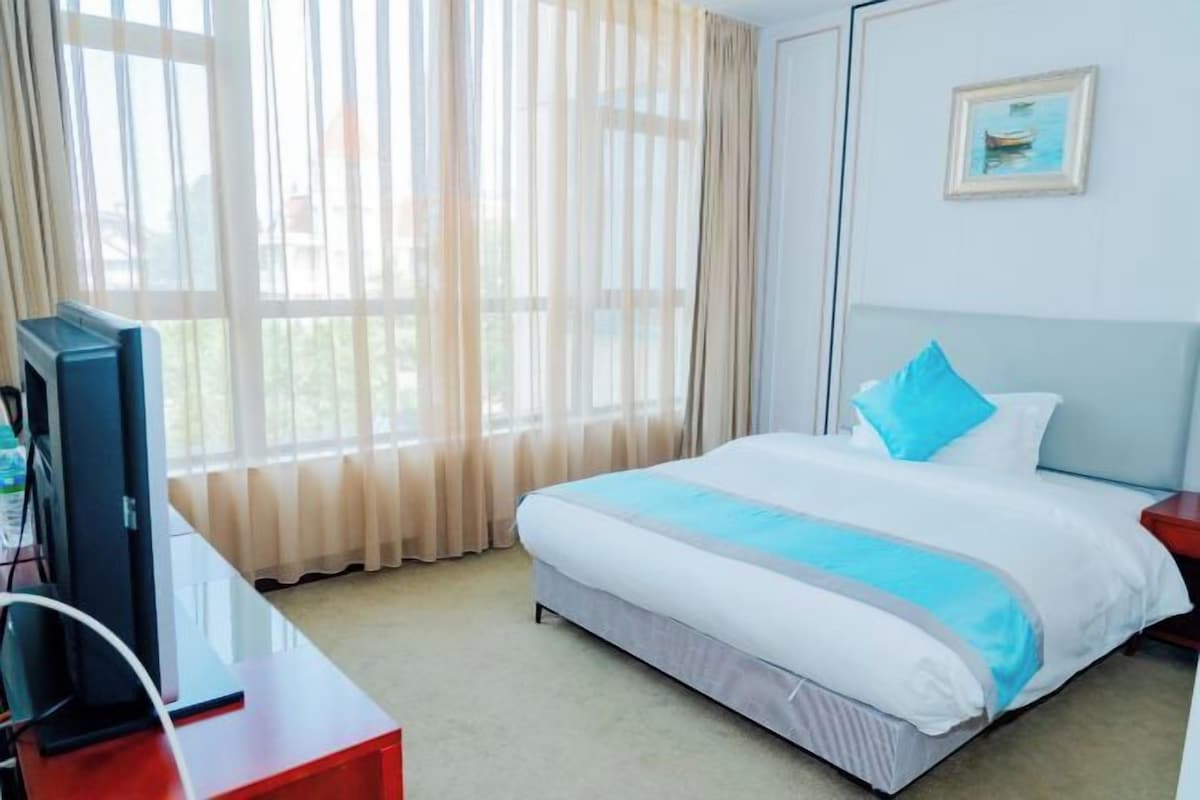 A hotel room with a bed, a desk with a computer, a television, and a window with curtains.