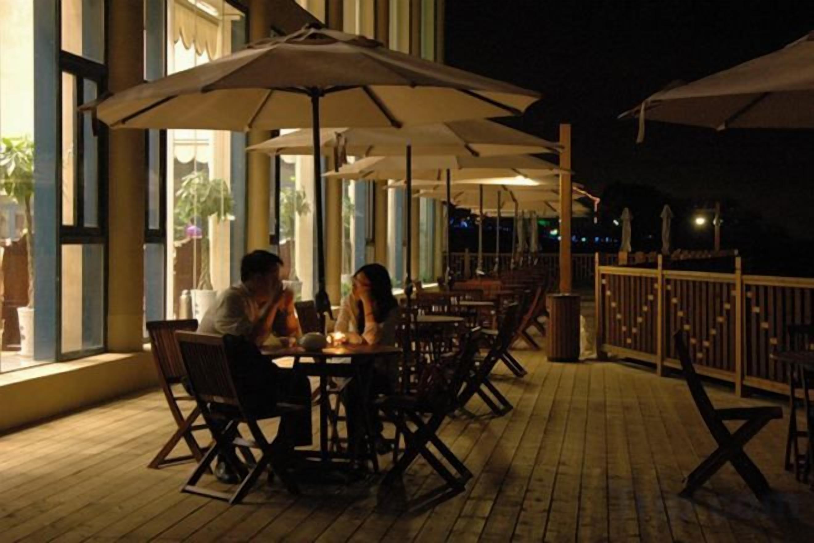 An outdoor dining area with tables and chairs, umbrellas, and a wooden deck.
