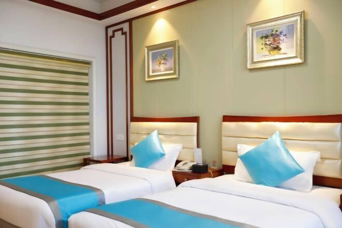 Una camera d'albergo con due letti, una tenda a righe alla finestra e due quadri appesi al muro.