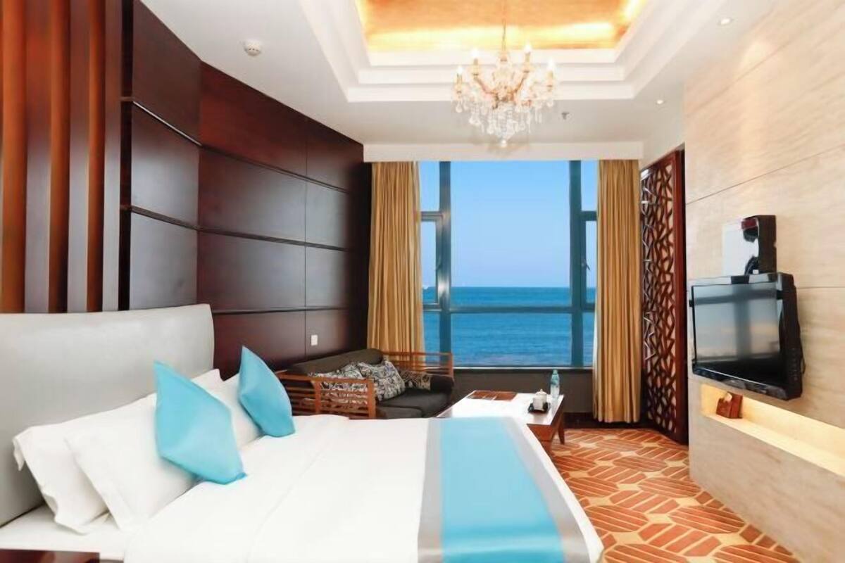 Una camera d'albergo con un letto grande, una TV, un'area salotto e vista sull'oceano.