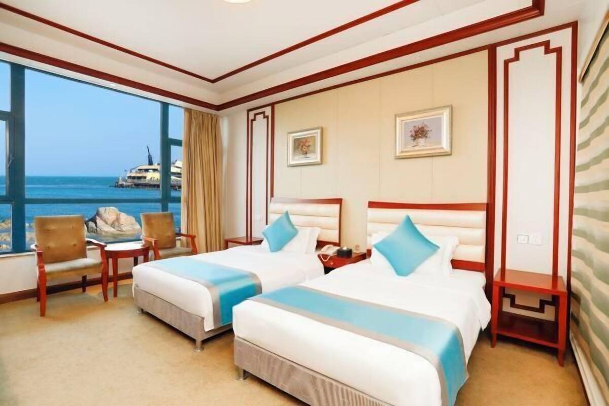Una camera d'albergo con due letti, vista mare e un balcone con una sedia.