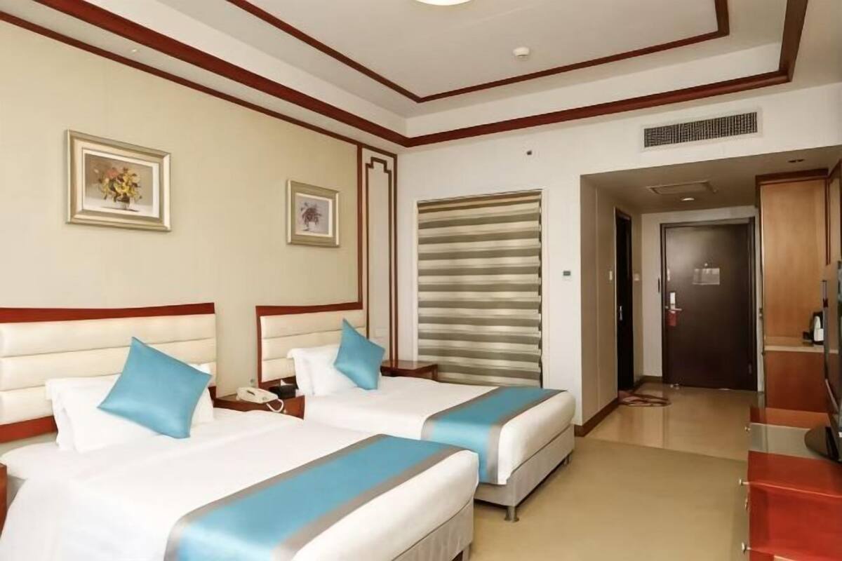 Camera d'albergo con due letti, un armadio in legno, una scrivania e una porta che dà su un'altra stanza.