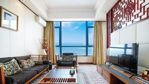 A modern living room with a sofa, armchair, coffee table, TV, and a large window with a view. - Beidaihe Bei Hua Yuan Sea View Hotel (Beidaihe Biluo Tower) (Qinhuangdao)