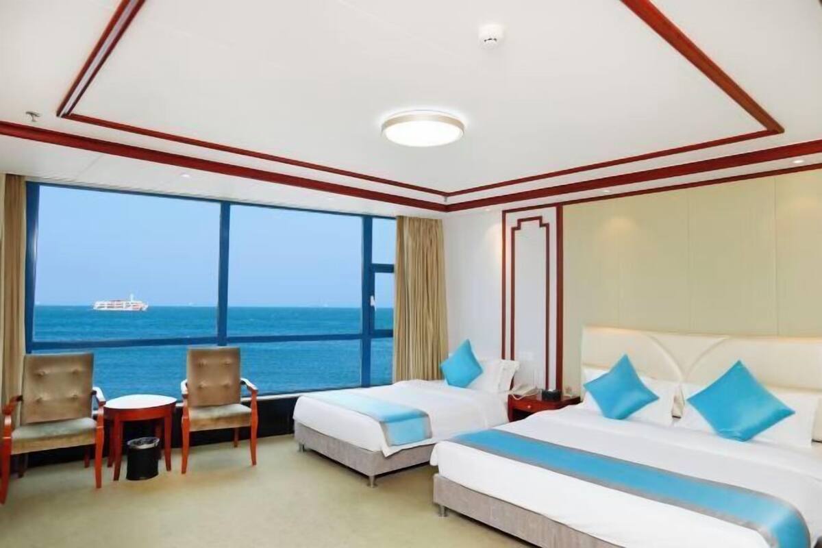 Una camera d'albergo con due letti, vista sul mare e una nave all'orizzonte.