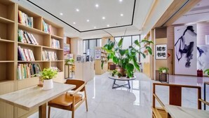 A modern library with bookshelves, a central table with chairs, and a large potted plant. - Timeless Hotel (Yantai)