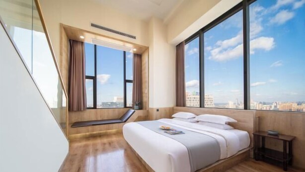 A modern bedroom with a large bed, a window with curtains, and a view of the cityscape. - Timeless Hotel (Yantai)