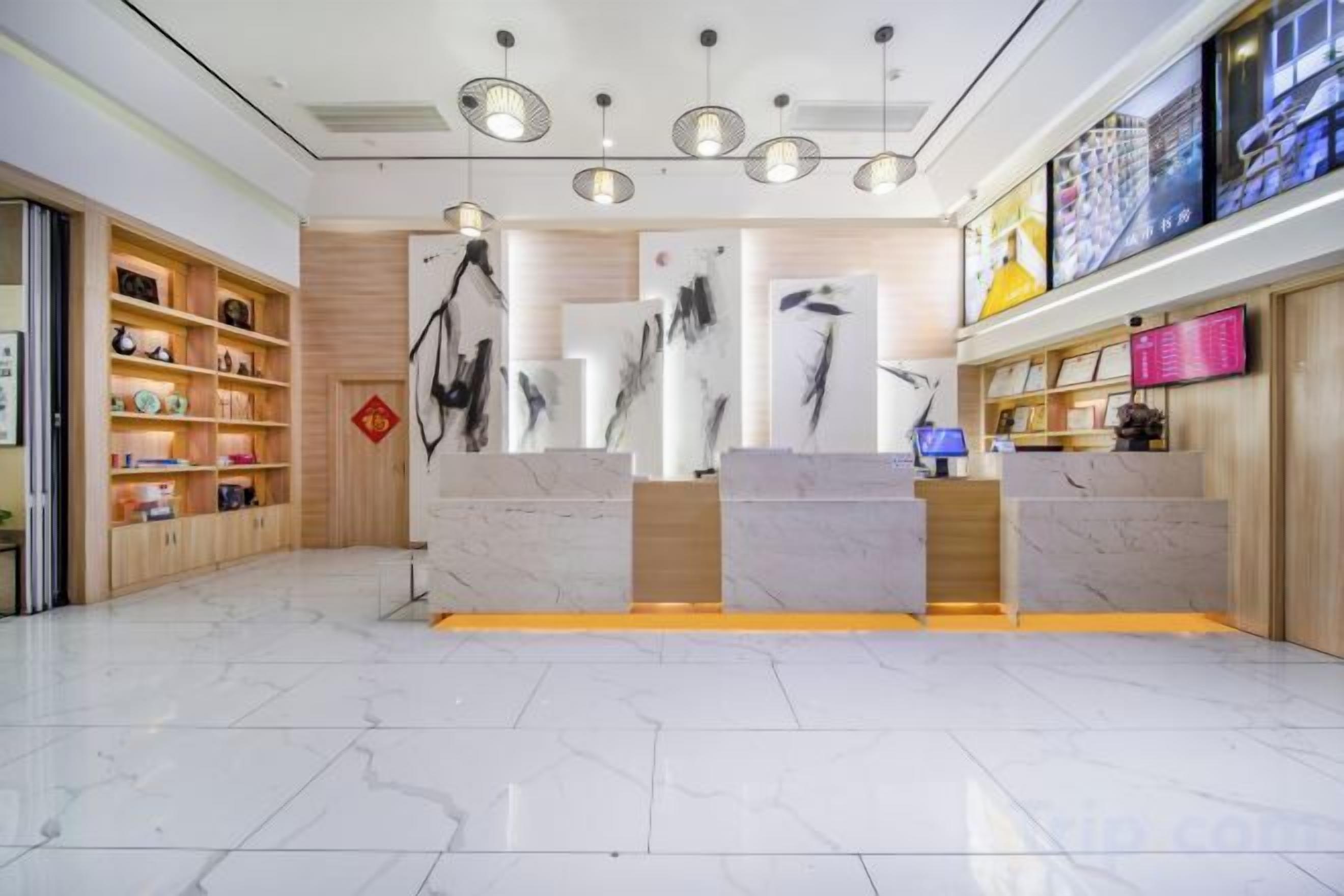 Zona de recepción de un hotel con piso de mármol, mostrador de madera y estantes con diversos objetos.