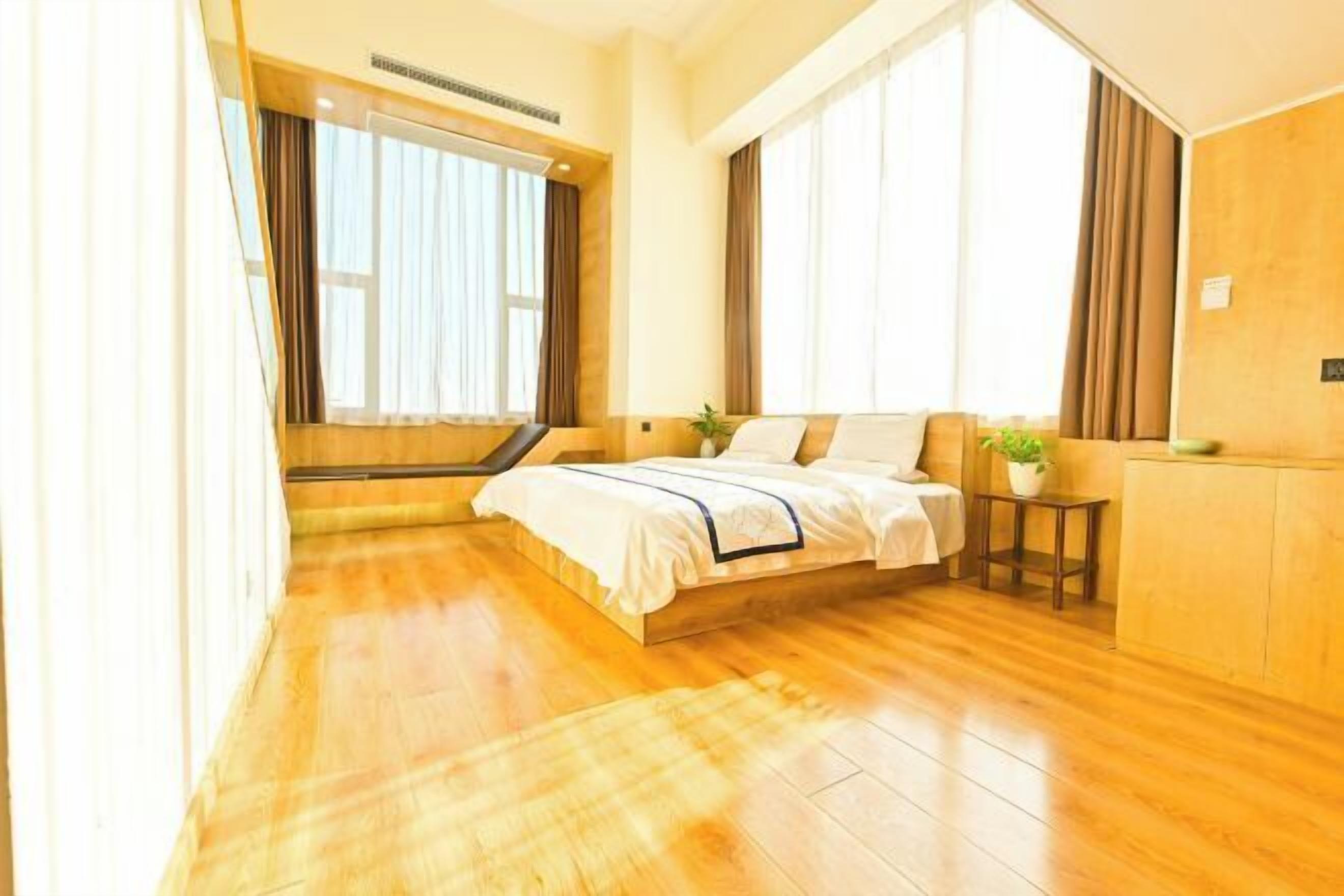 A bedroom with a bed, a small table with a plant, and a window with curtains.