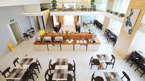 A spacious hotel lobby with a central reception desk, multiple dining areas, and a second-floor balcony with plants. - Timeless Hotel (Yantai)
