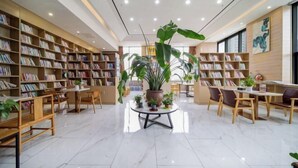 A spacious library with bookshelves, tables, chairs, and potted plants. - Timeless Hotel (Yantai)